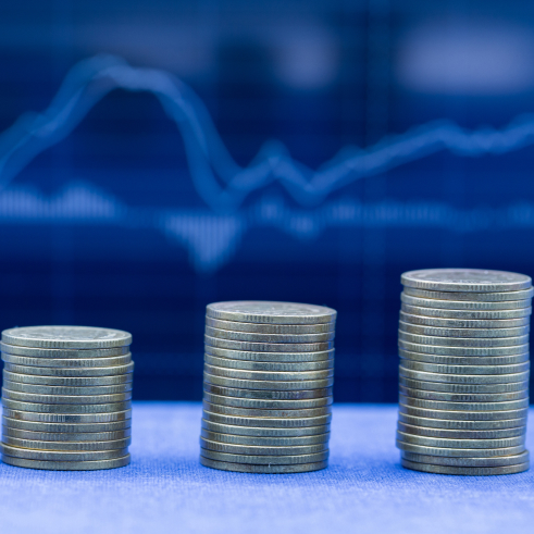 Increasing stacks of coins against a backdrop of a financial graph.